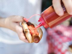 a person putting ketchup on the hot dog
