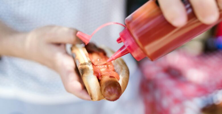 a person putting ketchup on the hot dog
